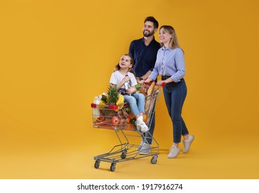 Happy family with shopping cart full of groceries on yellow background - Shutterstock ID 1917916274