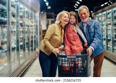 Happy family shopping at supermarket. Grandparents driving their grandchild in shopping cart and buying groceries