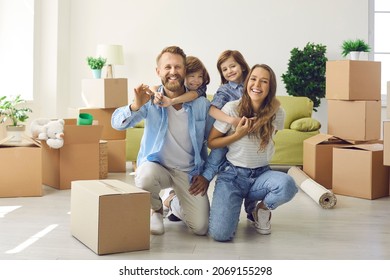 Happy family showing keys to new home on moving day. Portrait of mum, little kids and dad looking at camera and laughing in living room with unpacked cardboard boxes. Buying house or apartment concept