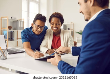 Happy family signing contract after consulting with real estate agent or mortgage broker. Mixed race couple at office desk together putting signatures on contract of sale or notary rent agreement - Powered by Shutterstock