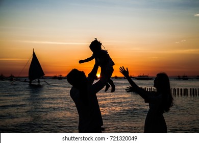 Happy Family - Silhouette Of Father Tossing Baby Girl And Mother On Sunset Sea . Philiphines.