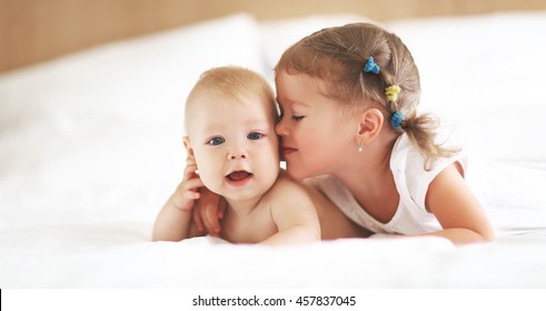 Happy Family Sister Kisses Baby Brother In Bed