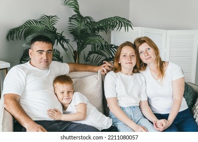 Happy Family Sits On The Sofa At Home. Dad, Mom, Teenage Daughter And Son Hugging And Having A Good Time Together. The Family Moved Into A New Apartment.