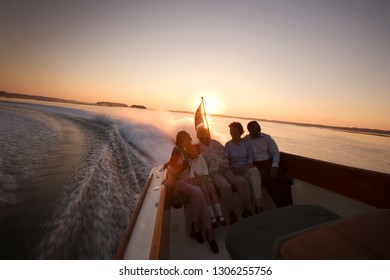 Happy Family Sitting In The Back Of A Jet Boat On The Water At Sunset.