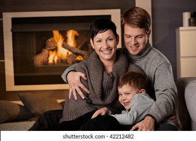 Happy Family Sitting On Couch At Home In A Cold Winter Day, Looking At Camera, Smiling.