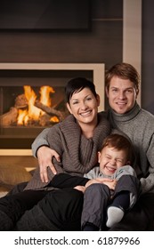 Happy Family Sitting On Couch At Home In A Cold Winter Day, Looking At Camera, Laughing.