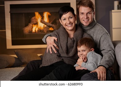 Happy Family Sitting On Couch At Home In A Cold Winter Day, Looking At Camera, Smiling.