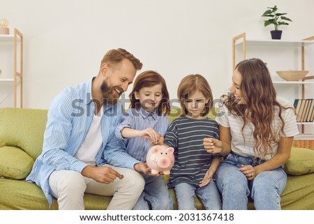 Happy family sitting on cozy sofa at home and putting coins inside piggy bank. Cheerful thrifty couple teaching their children money management. Cute little kids learning to save up and spend wisely