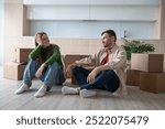 Happy family sitting on floor of new home after moving in. Smiling couple bought new apartment, investment in real estate, relocation, rental property, new beginning, mortgage loan for young family