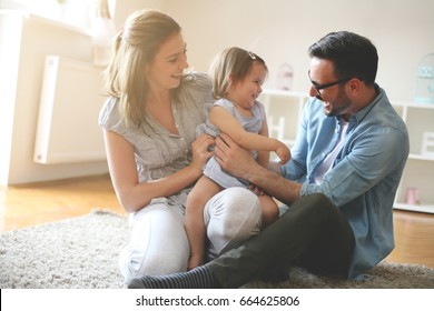 Happy family sitting on floor with their little baby. Family spending time at home with their daughter. - Powered by Shutterstock