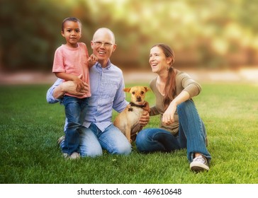 Happy Family Sitting On Grass In Yard With Multi-ethnic Child And Dog