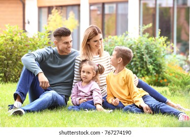 Happy family sitting on green grass in courtyard near their house - Powered by Shutterstock