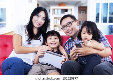 Happy Family Sitting On Red Sofa At Home