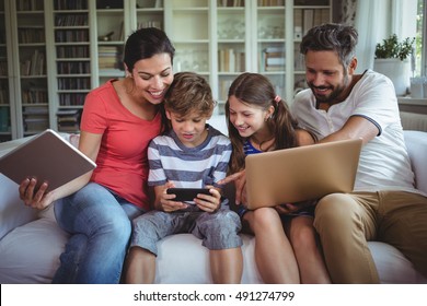 Fröhliche Familie sitzt auf Sofa und nutzt Laptop, Handy und digitale Tablette zu Hause