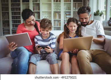 Happy family sitting on sofa and using laptop, mobile phone and digital tablet at home - Shutterstock ID 491275021