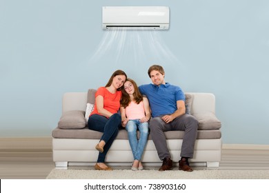 Happy Family Sitting On Sofa Under Air Conditioning At Home