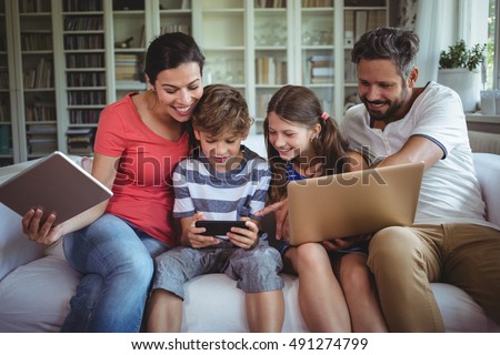 Happy family sitting on sofa and using laptop, mobile phone and digital tablet at home