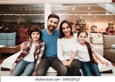 Happy family sitting on soft mattress in orthopedic furniture store. Healthy posture concept. Testing softness of mattress. Choosing mattress in store