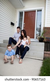 Happy Family Sitting On Steps In Front Of House