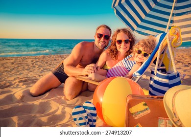 Happy Family Sitting On The Sunbed. Man, Woman And Child Having Fun At The Beach. Summer Vacation Concept