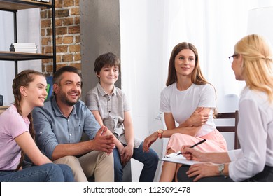 happy family sitting on therapy session by female counselor writing in clipboard in office 