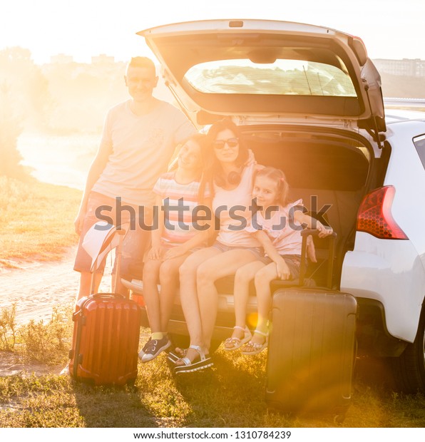 Happy family sitting on a trunk of a car holding\
suitcases on a travel\
vacation
