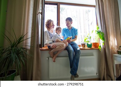 Happy family sitting on a window sill and read a book. - Powered by Shutterstock