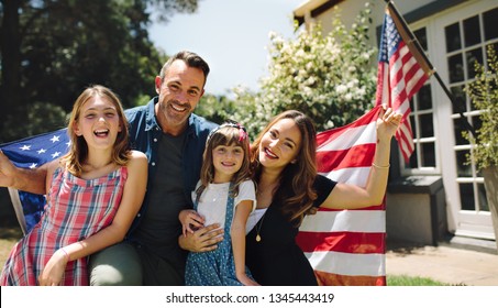 Happy family sitting together in their backyard holding the american flag behind them. Smiling couple with their kids celebrating american independence day holding american flag. - Powered by Shutterstock