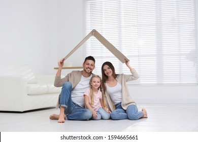 Happy Family Sitting Under Cardboard Roof At Home. Insurance Concept