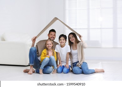 Happy Family Sitting Under Cardboard Roof At Home. Insurance Concept