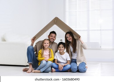 Happy Family Sitting Under Cardboard Roof At Home. Insurance Concept