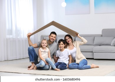 Happy Family Sitting Under Cardboard Roof At Home. Insurance Concept