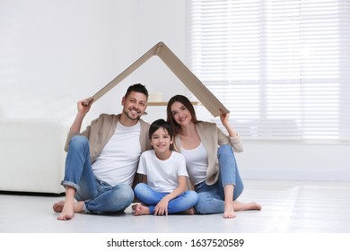 Happy Family Sitting Under Cardboard Roof At Home. Insurance Concept