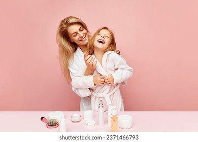Happy family. Smiling daughter, little girl and young beautiful mother, woman with cosmetic jars, comb on table having fun over pastel pink background. Concept of fashion, beauty, treatment, bathroom. - Powered by Shutterstock