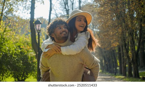 Happy family smiling multiracial couple Hispanic girlfriend woman female piggyback ride point finger Indian man boyfriend male in love touching hugging speak talk walking in park date nature outdoors - Powered by Shutterstock