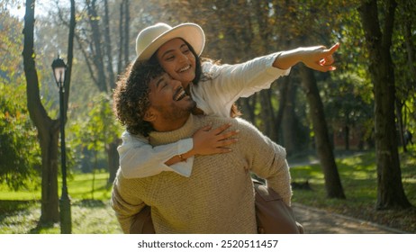 Happy family smiling multiracial couple Hispanic girlfriend woman female piggyback ride point finger Indian man boyfriend male in love touching hugging speak talk walking in park date nature outdoors - Powered by Shutterstock