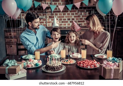 Happy Family Is Smiling While Sitting At The Table In Decorated Kitchen During Birthday Celebration, Kids Are Looking At Camera