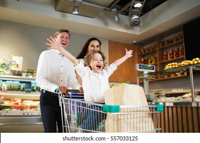 Fröhliche Familie und Sohn im Supermarkt.Junge lächelnde Eltern und ihr süßes Kind mit Einkaufswagen voller frischer Lebensmittel Spaß im Lebensmittelgeschäft, Junge sitzend im Einkaufswagen
