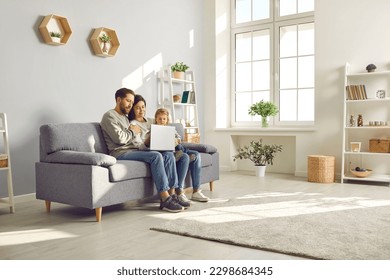 Happy family spend time in spacious room at home. Couple with child watch online movie on laptop sitting on sofa in cozy light living place space with white grey walls, shelves, house plants and wifi - Powered by Shutterstock