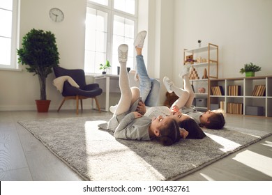 Happy Family Spending Leisure Time At Home. Carefree, Cheerful Young Mother And Children Lying On Warm Floor Rug In Their Apartment. Mum And Kids Relaxing On Soft Carpet In Cosy Sunny Living Room