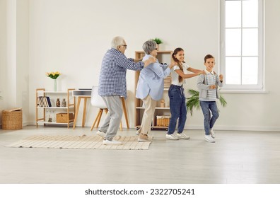 Happy family spending time at home and having fun together. Funny grandparents and children play games and dance conga line. Little kids with granny and granddad walk in line like train in living room - Powered by Shutterstock