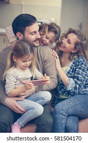 Happy Family Spending Time At Home And Looking Something On The Phone.