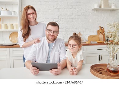 Happy family spending time together sitting at tablet in cozy sunny kitchen at home. Kitchen design, furniture for kitchen. Amicable, happy family. - Shutterstock ID 2147681467