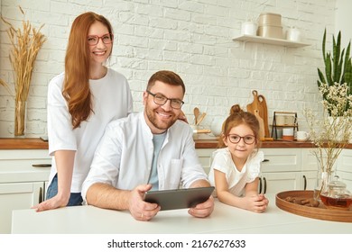 Happy family spending time together at a table in the sunny kitchen with an ipad tablet. Kitchen design, furniture for kitchen. Amicable, happy family. - Shutterstock ID 2167627633