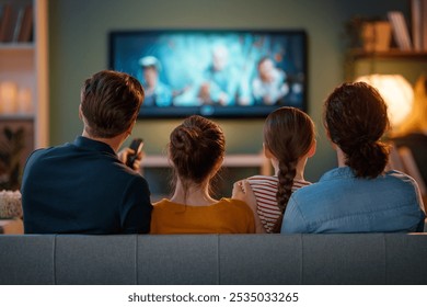 Happy family spending time together. Mother, father and children watching  TV, movies with popcorn in the evening at home.