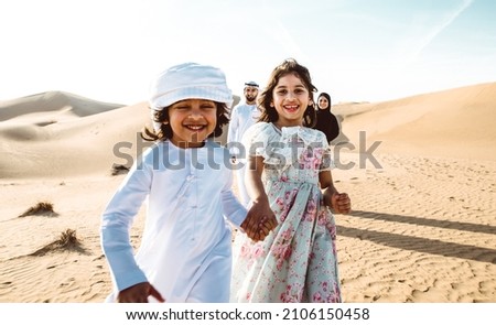 Happy family spending a wonderful day in the desert making a picnic. People from the emirates with traditional clothes making a safari in Dubai