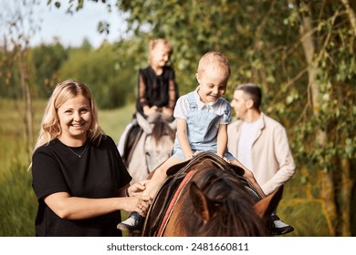 A happy family spends time with their children riding horses in the forest. A mother and her little son are smiling and looking at the camera. Selective focus. - Powered by Shutterstock