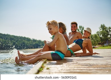 Happy Family Splashing Water With Their Feet At A Lake On Their Holidays