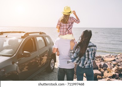 Happy family standing near a car on the beach. Happy family on a road trip in their car. Dad, mom and daughter are traveling by the sea or the ocean or the river. Summer ride by automobile