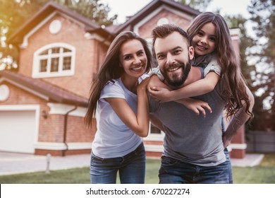 Happy family is standing near their modern house, smiling and looking at camera.